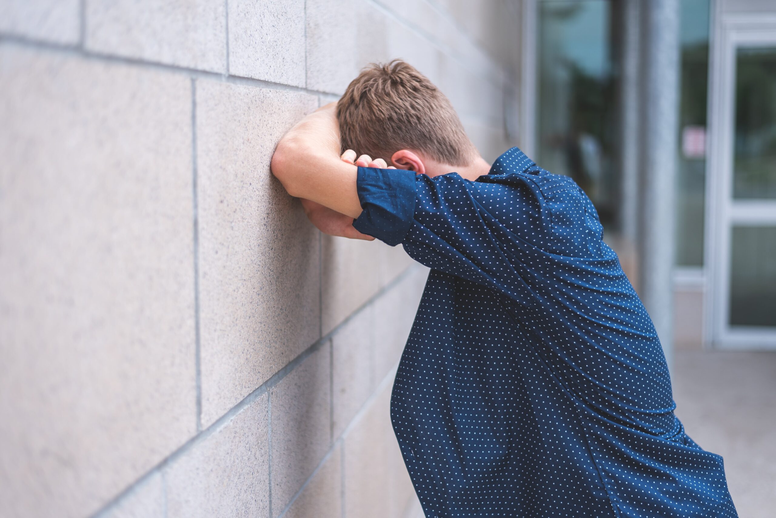 a teen with his head on wall stressed.